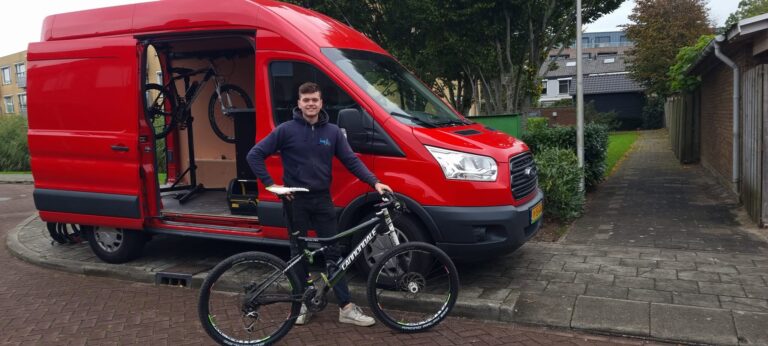 Sam Sleeuwenhoek bij zijn rode bus met een fiets