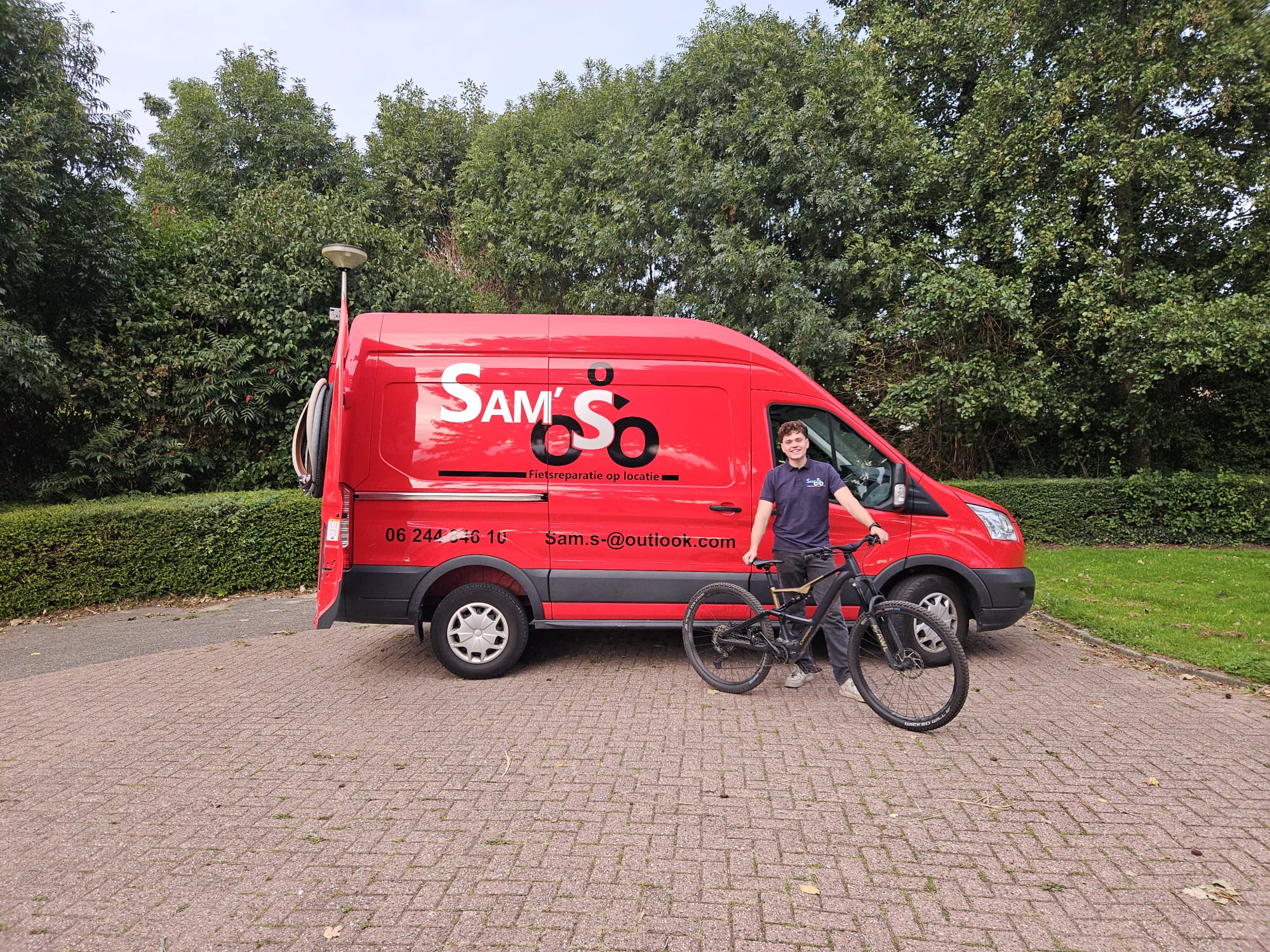 Sam Sleeuwenhoek met een fiets voor zijn rode bus